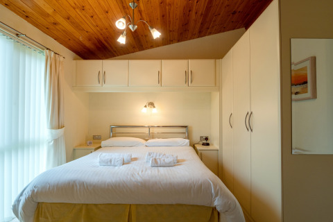 Slaapkamer in Whitsand Bay Lodge, VK, met tweepersoonsbed, houten plafond en inbouwkasten.
