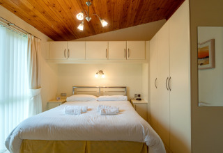 Slaapkamer in Whitsand Bay Lodge, VK, met tweepersoonsbed, houten plafond en inbouwkasten.