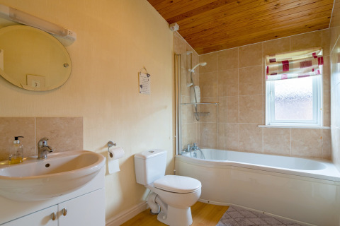 Modern lichte badkamer in Whitsand Bay Lodge, VK, met ligbad, houten plafond en betegelde wanden.