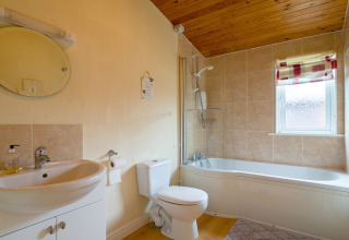 Modern lichte badkamer in Whitsand Bay Lodge, VK, met ligbad, houten plafond en betegelde wanden.