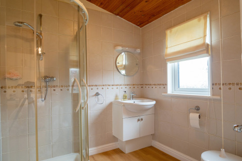 Moderne badkamer met glazen douche, houten plafond en raam in Whitsand Bay Lodge, Verenigd Koninkrijk.