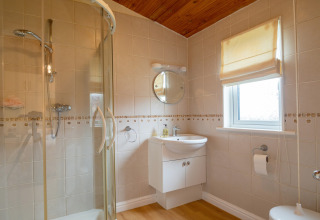 Moderne badkamer met glazen douche, houten plafond en raam in Whitsand Bay Lodge, Verenigd Koninkrijk.