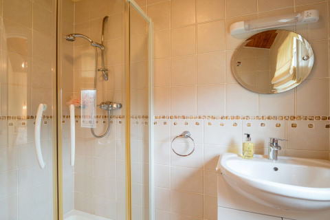 Badkamer in Whitsand Bay Lodge, VK, met douchecabine, ronde wandspiegel en witte wastafel.