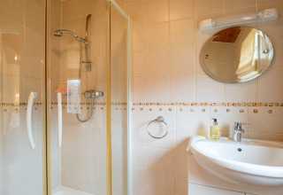 Badkamer in Whitsand Bay Lodge, VK, met douchecabine, ronde wandspiegel en witte wastafel.