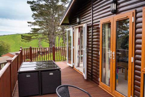 Buitenterras bij Whitsand Bay Lodge in het VK, met houten meubels en uitzicht op groene heuvels.