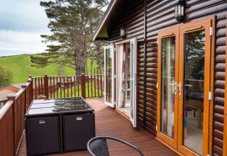 Buitenterras bij Whitsand Bay Lodge in het VK, met houten meubels en uitzicht op groene heuvels.
