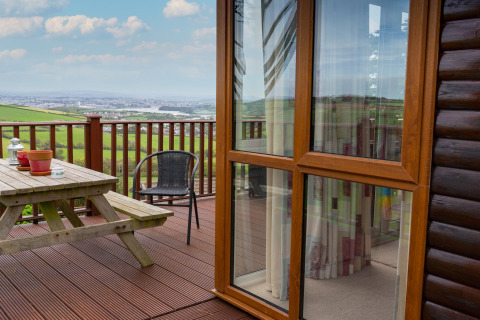 Houten terras met picknicktafel en uitzicht op landschap bij Whitsand Bay Lodge, Verenigd Koninkrijk, zonnige dag.