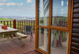 Houten terras met picknicktafel en uitzicht op landschap bij Whitsand Bay Lodge, Verenigd Koninkrijk, zonnige dag.