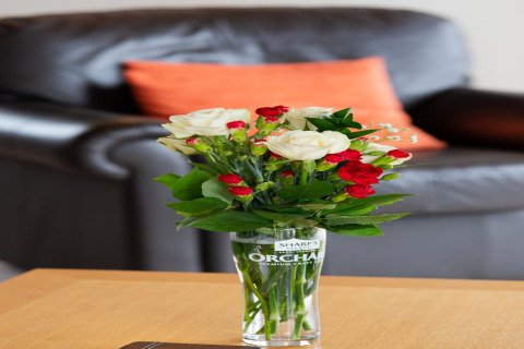 Een boeket witte en rode bloemen in een glas op een tafel voor een zwarte bank in Whitsand Bay Lodge.