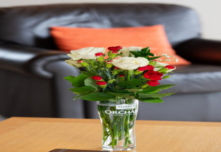 Een boeket witte en rode bloemen in een glas op een tafel voor een zwarte bank in Whitsand Bay Lodge.