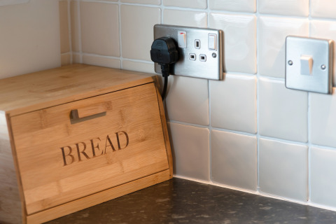 Keukenhoek met houten broodtrommel, witte tegels en stopcontacten in Whitsand Bay Lodge.