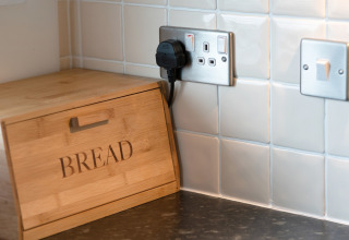 Keukenhoek met houten broodtrommel, witte tegels en stopcontacten in Whitsand Bay Lodge.