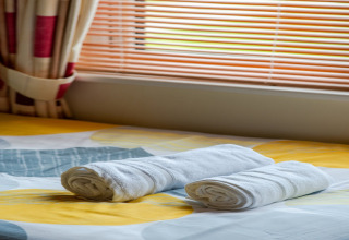 Kamer in Whitsand Bay Lodge met twee opgerolde witte handdoeken op een bed onder een raam met jaloezieën.