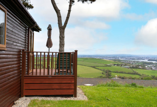 Houten lodge met terras en uitzicht op groene velden bij Whitsand Bay Lodge in het Verenigd Koninkrijk.