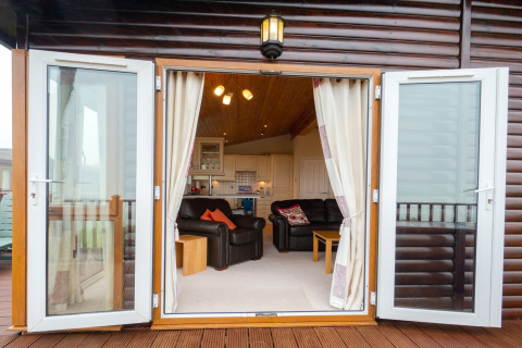 Open glazen deuren naar lounge en keuken in Whitsand Bay Lodge, Verenigd Koninkrijk, houten afwerking zichtbaar.