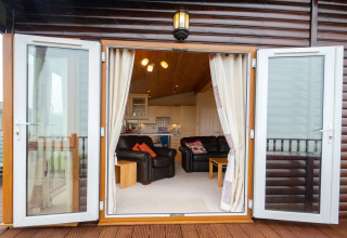 Open glazen deuren naar lounge en keuken in Whitsand Bay Lodge, Verenigd Koninkrijk, houten afwerking zichtbaar.