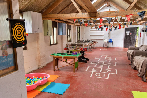 Area giochi interna in un teepee con vasca di palline, bersaglio, mini biliardo, divani e festoni colorati.