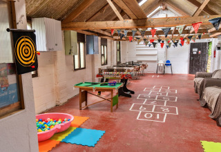 Area giochi interna in un teepee con vasca di palline, bersaglio, mini biliardo, divani e festoni colorati.