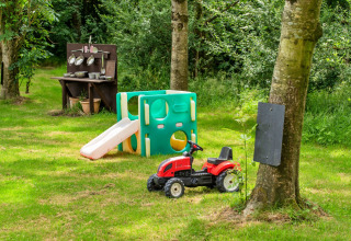Area giochi per bambini in giardino con scivolo, cucina giocattolo e trattore rosso tra gli alberi.
