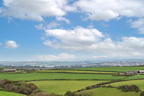 Panoramisch uitzicht op groene velden en landschap vanaf Whitsand Bay Lodge in het Verenigd Koninkrijk onder blauwe lucht.