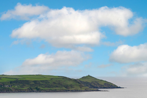 Kustlandschap met groene velden en heuvels, gezien vanaf Whitsand Bay Lodge, VK, onder blauwe lucht.