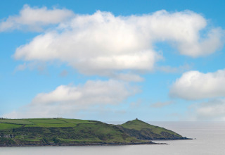 Kustlandschap met groene velden en heuvels, gezien vanaf Whitsand Bay Lodge, VK, onder blauwe lucht.