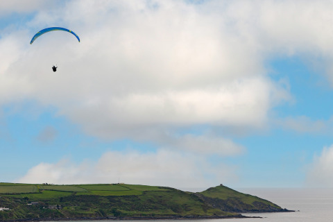 Een paraglider zweeft boven de groene heuvels en kust bij Whitsand Bay Lodge in het Verenigd Koninkrijk.