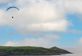 Een paraglider zweeft boven de groene heuvels en kust bij Whitsand Bay Lodge in het Verenigd Koninkrijk.