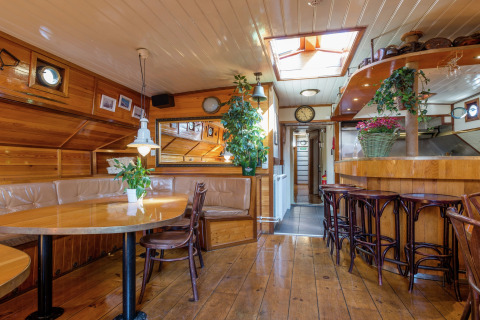 Interieur van woonboot in Leiden met houtpanelen, planten, eethoek en bar dicht bij het centrum.
