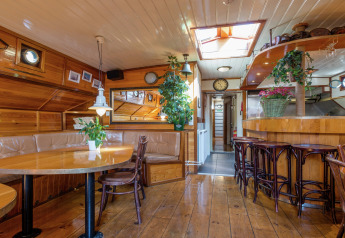 Interior de casa flotante en Leiden con paneles de madera, plantas, comedor y barra cerca del centro.