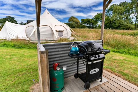 Foto di una spaziosa tenda tipi nella natura con barbecue e bombola del gas in primo piano.