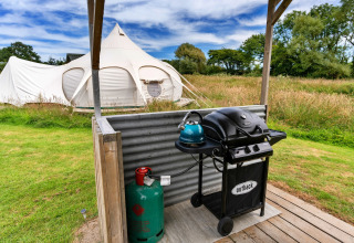 Foto di una spaziosa tenda tipi nella natura con barbecue e bombola del gas in primo piano.