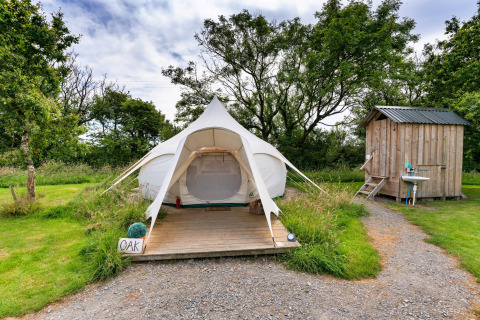 Foto di una tenda tipi Oak Lotus Belle con pedana in legno e una piccola casetta in un campeggio verde.
