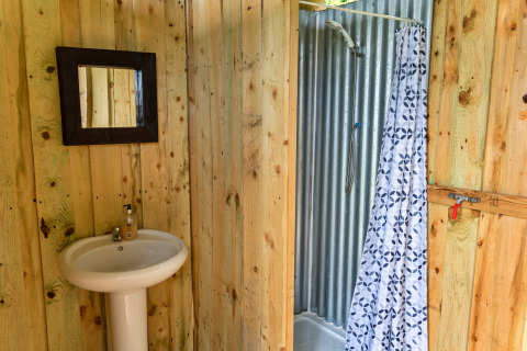 Bagno rustico in una tenda tipi con pareti in legno, specchio, lavabo bianco e doccia con tenda.