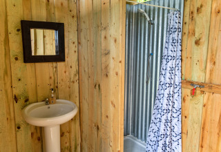 Bagno rustico in una tenda tipi con pareti in legno, specchio, lavabo bianco e doccia con tenda.