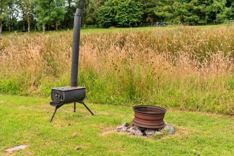 Scena all'aperto all'Oak Lotus Belle Teepee nel Regno Unito con stufa a legna e focolare sull'erba.