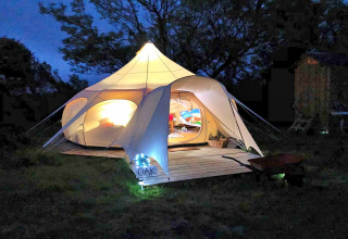 Tenda tipi Oak Lotus Belle illuminata nel Regno Unito di notte, atmosfera accogliente e alberi sullo sfondo.