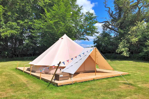 The 'Lilypad Bell Tent', a teepee-style tent, set on a wooden platform in a grassy field in the UK.