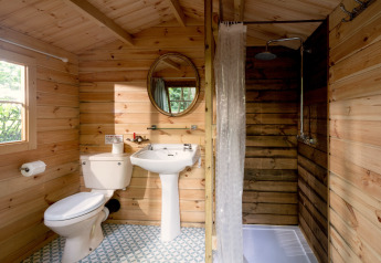 Wood-paneled bathroom at Daisy Glamping Pod, UK, featuring a toilet, sink, and shower with natural light.