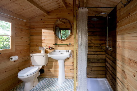 Houten badkamer in Daisy Glamping Pod, VK, met toilet, wastafel en douche, verlicht door natuurlijk licht.