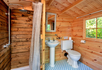 Bathroom with wooden walls, shower, pedestal sink, and toilet inside Daisy Glamping Pod, United Kingdom.