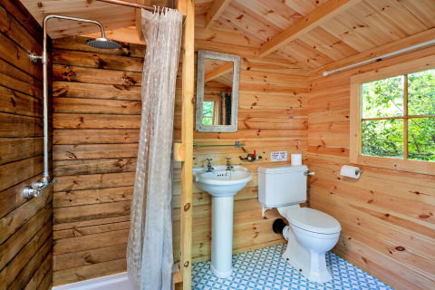 Badkamer met houten wanden, douche, wastafel en toilet in Daisy Glamping Pod, Verenigd Koninkrijk.