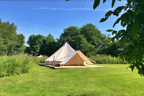 A large Lilypad Bell Tent sits on green grass, surrounded by trees under a clear blue sky in the UK.