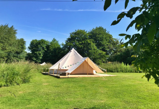 A large Lilypad Bell Tent sits on green grass, surrounded by trees under a clear blue sky in the UK.