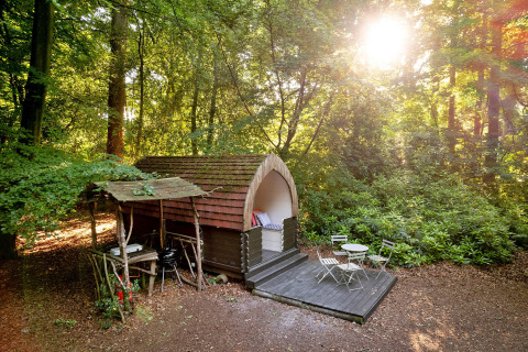 Daisy Glamping Pod in een zonnige bosrijke omgeving in het Verenigd Koninkrijk, met terras en stoelen.