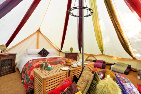 Farverig indretning i Bedouin Bell Tent med dobbeltseng, puder og tæpper, Storbritannien, glamping.