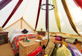 Farverig indretning i Bedouin Bell Tent med dobbeltseng, puder og tæpper, Storbritannien, glamping.