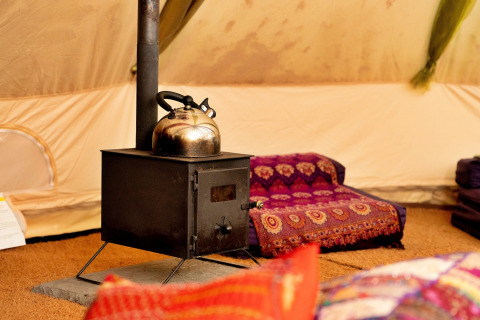 Inde i en Bedouin Bell telt, ses en komfur med tekande og farverige puder i et hyggeligt hjørne.