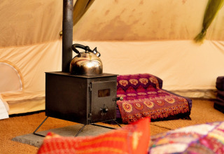 Inde i en Bedouin Bell telt, ses en komfur med tekande og farverige puder i et hyggeligt hjørne.