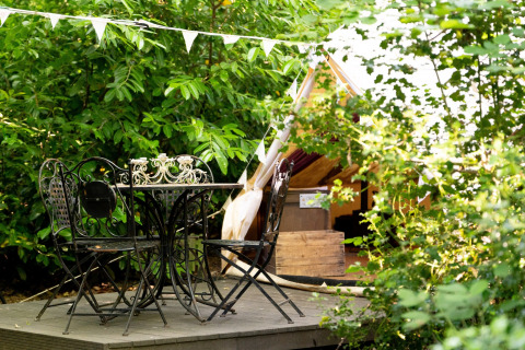 Udendørs plateu med sort smedejernsbord og stole foran et Bedouin Bell Tent, omgivet af grønne planter.